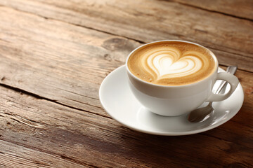 Obraz premium A white cup of coffee with heart-shaped latte art on a wooden table next to a small spoon.
