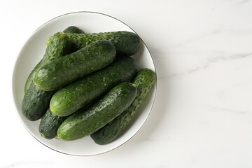 Fresh cucumbers in bowl on white marble table, top view. Space for text