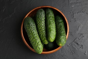 Fresh cucumbers in bowl on dark textured table, top view