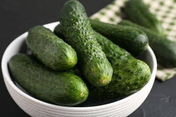 Fresh cucumbers in bowl on dark textured table, closeup