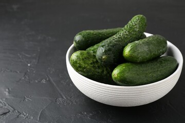Fresh cucumbers in bowl on dark textured table, closeup. Space for text