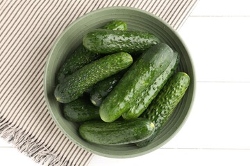 Fresh cucumbers in bowl on white wooden table, top view
