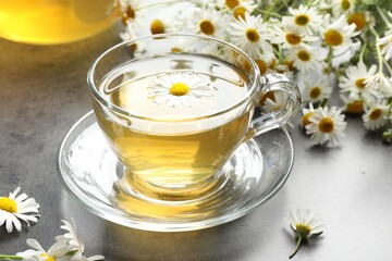 Tasty chamomile tea and flowers on grey table, closeup