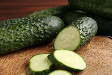 Whole and cut cucumbers on wooden table, closeup
