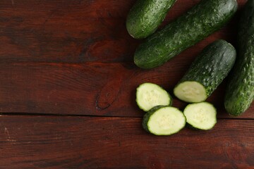 Whole and cut cucumbers on wooden table, flat lay. Space for text