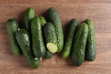 Whole and cut cucumbers on wooden table, flat lay