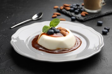 Tasty panna cotta with blueberries, almonds and sauce on black table, closeup