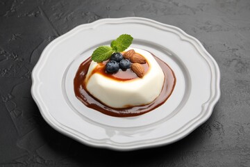 Tasty panna cotta with blueberries, almonds and sauce on black table, closeup