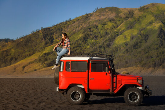 Side view of a woman sitting on the roof of a jeep parked by Mt Bromo, Bromo Tengger Semeru National Park, East Java, Indonesia