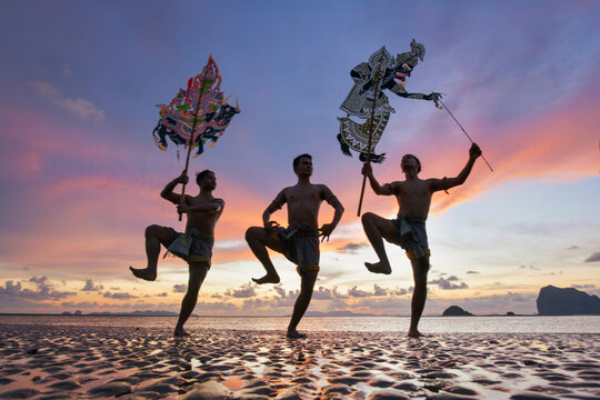 Silhouette of three men performing Traditional Thai Shadow Puppet Show (Nang Talung) on a beach at sunrise, Thailand