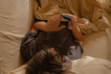 13 year old boy relaxing on sofa and using smartphone at home in the afternoon