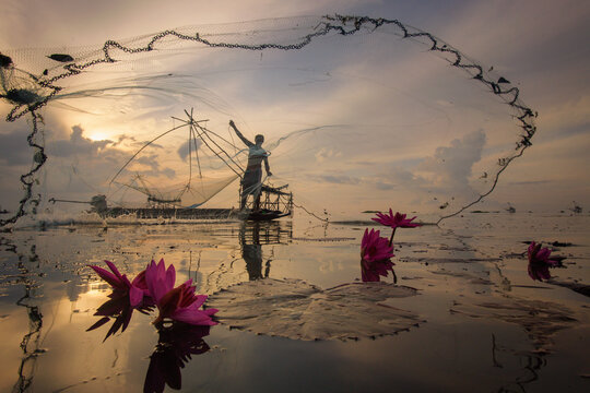 Silhouette of a fisherman standing on a boat casting his fishing net at sunrise, Bang Phra reservoir (Bangpra Lake), Chon Buri, Thailand