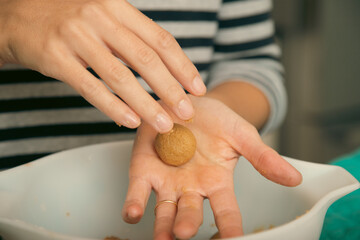 Close-up of a mid adult woman standing in a kitchen rolling balls of cookie dough in her hand
