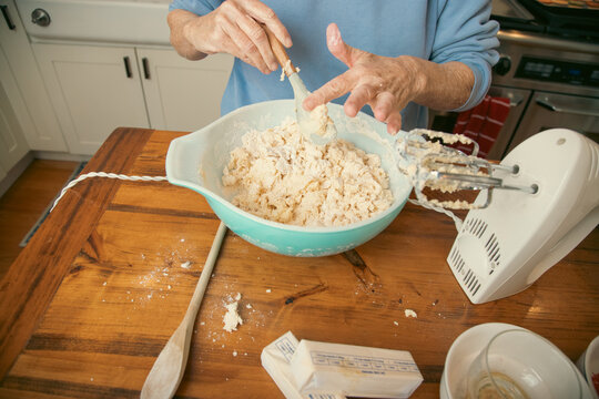 Close-up of a senior woman standing in a kitchen scraping cookie dough off a spatula with her finger