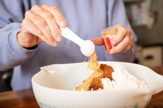 Close-up of a senior woman standing in a kitchen adding spices to a bowl of flour to make cookies