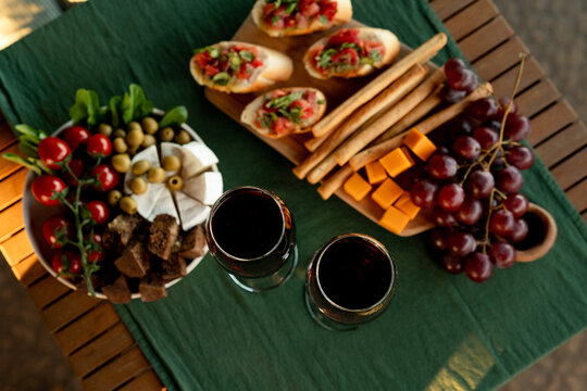 Overhead view of two glasses of red wine with tomato bruschetta, cheese, olives, grapes and breadsticks on a garden table