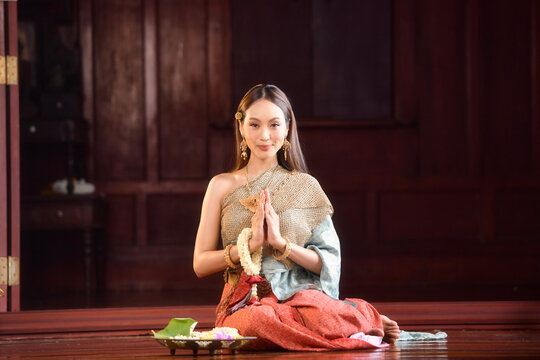Portrait of a young woman wearing traditional Thai clothing sitting on the floor with religious offerings praying
