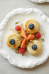 Syrniki pancakes with berries and crushed pistachios on elegant plate