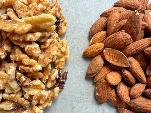 Close-up overhead view of a stack of walnuts next to a stack of almonds on a kitchen worktop