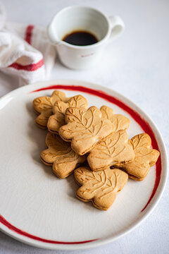Close-up of a plate of traditional Canadian maple leaf shaped cookies with a jug of maple syrup
