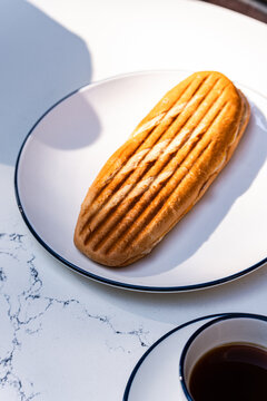 Close-up of a toasted cheese panini sandwich and a cup of black coffee on marble table