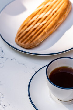 Close-up of a toasted cheese panini sandwich and a cup of black coffee on marble table