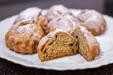 Freshly baked muffins are laid out on a white plate, revealing the inside of one muffin after being sliced and dusted with powdered sugar