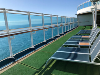 View of vibrant blue sky and sea through a sleek contemporary balcony of a cruise ship, with contemporary sun lounges lined up on a bright sunny day