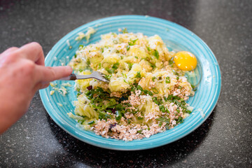 Hand mixing grated zucchini, oats, herbs and egg on blue plate preparing healthy dish. Zucchini pancakes
