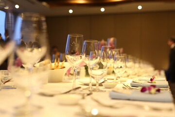 Elegant indoor banquet setup with warm lighting, neatly arranged glassware, folded napkins, and floral accents — perfect for a formal event or celebration.