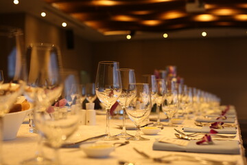 Elegant indoor banquet setup with warm lighting, neatly arranged glassware, folded napkins, and floral accents — perfect for a formal event or celebration.