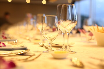 Elegant indoor banquet setup with warm lighting, neatly arranged glassware, folded napkins, and floral accents — perfect for a formal event or celebration.