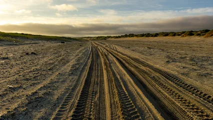 Fototapete Eisenbahnlinie Tire tracks on sandy beach landscape at sunset, showcasing natural textures and patterns, with gentle waves in the distance and a serene atmosphere of tranquility and exploration  © Denis Tuev