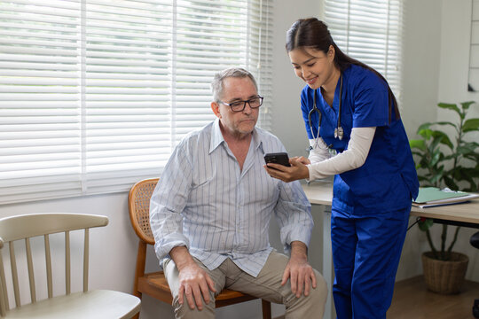Elderly care. Friendly female caregiver shows elderly woman how to use modern mobile applications to monitor her health. Nurse and senior man in nursing home are looking at mobile phone screen.