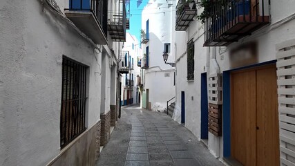 Whitewashed walls and blue windows line a narrow street in Peniscola, Spain