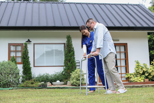 Nurse talking to an elderly man with a walker for the elderly old man goes for a walk encouragement and care in residential setting with green grass and houses in background