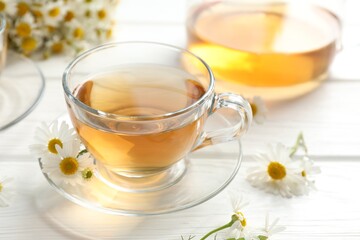 Aromatic tea in glass cups and chamomile flowers on white wooden table, closeup
