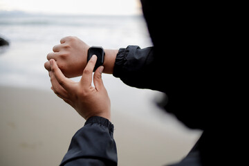 An athlete wears a smartwatch on his arm, is running and using an app. A male trainer in sportswear...