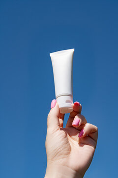 Woman's hand holding cosmetic tube against blue sky