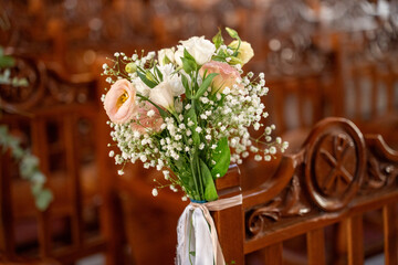 Beautiful floral arrangement adorning wooden chairs in a sunlit venue before a romantic wedding ceremony