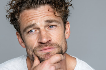 Close-up of a pensive middle-aged man with curly hair and blue eyes on gray background