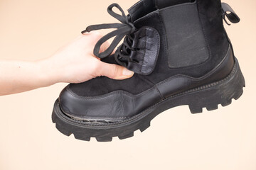 Torn boots held by a hand showcasing wear and tear after extensive use in outdoor activities or urban environments