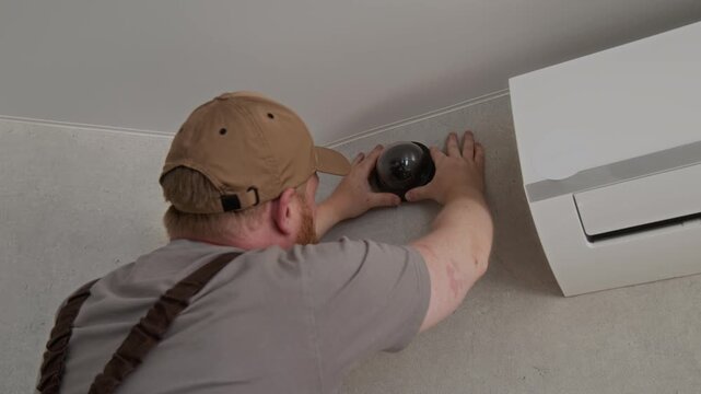 Back view of Caucasian worker installing CCTV camera in apartment updating home security system for client