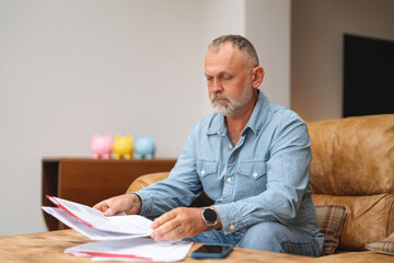 Man reviewing financial documents while sitting on a couch in a cozy living room during the daytime