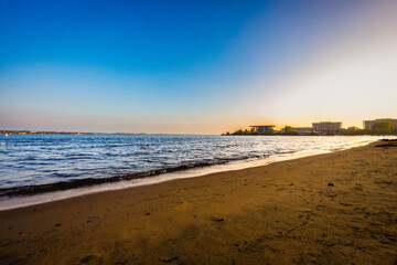Beach at sunset with calm water and soft sand visible.