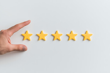 A hand adding a fifth star to a row of yellow stars, representing excellent feedback or rating on a pristine white background. Full score achieved.