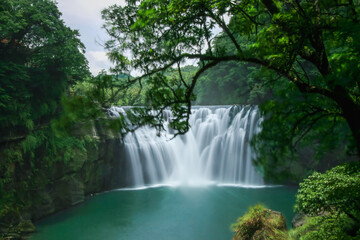 Naklejka premium Stunning Shifen Waterfall in Pingxi District, New Taipei City, surrounded by lush greenery, captured on a summer day in 2010 with clear blue skies.