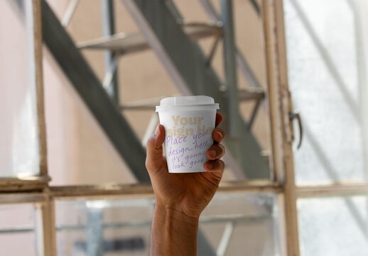 Mockup of Hand Holding take away coffee Cup by Window