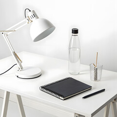 Modern white desk setup with adjustable lamp notebook pen and water bottle on a clean white surface
