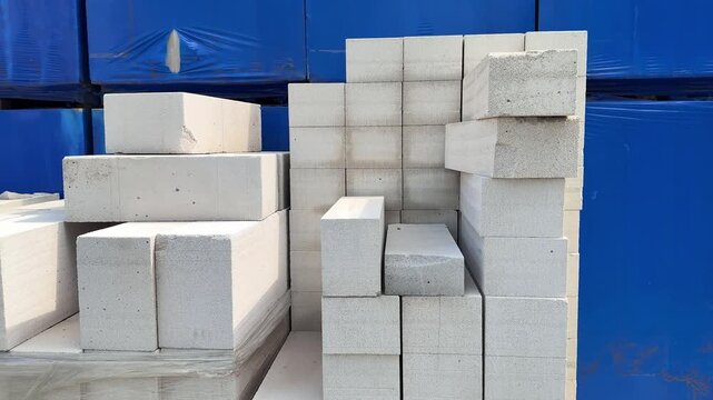 White lightweight aerated concrete blocks rotating slowly on wooden pallet, revealing structural variations and architectural potential against clean blue industrial background